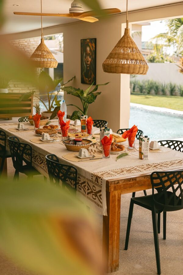 Grande tablée dressée avec serviettes orange et lanternes, ouverte sur le jardin et la piscine